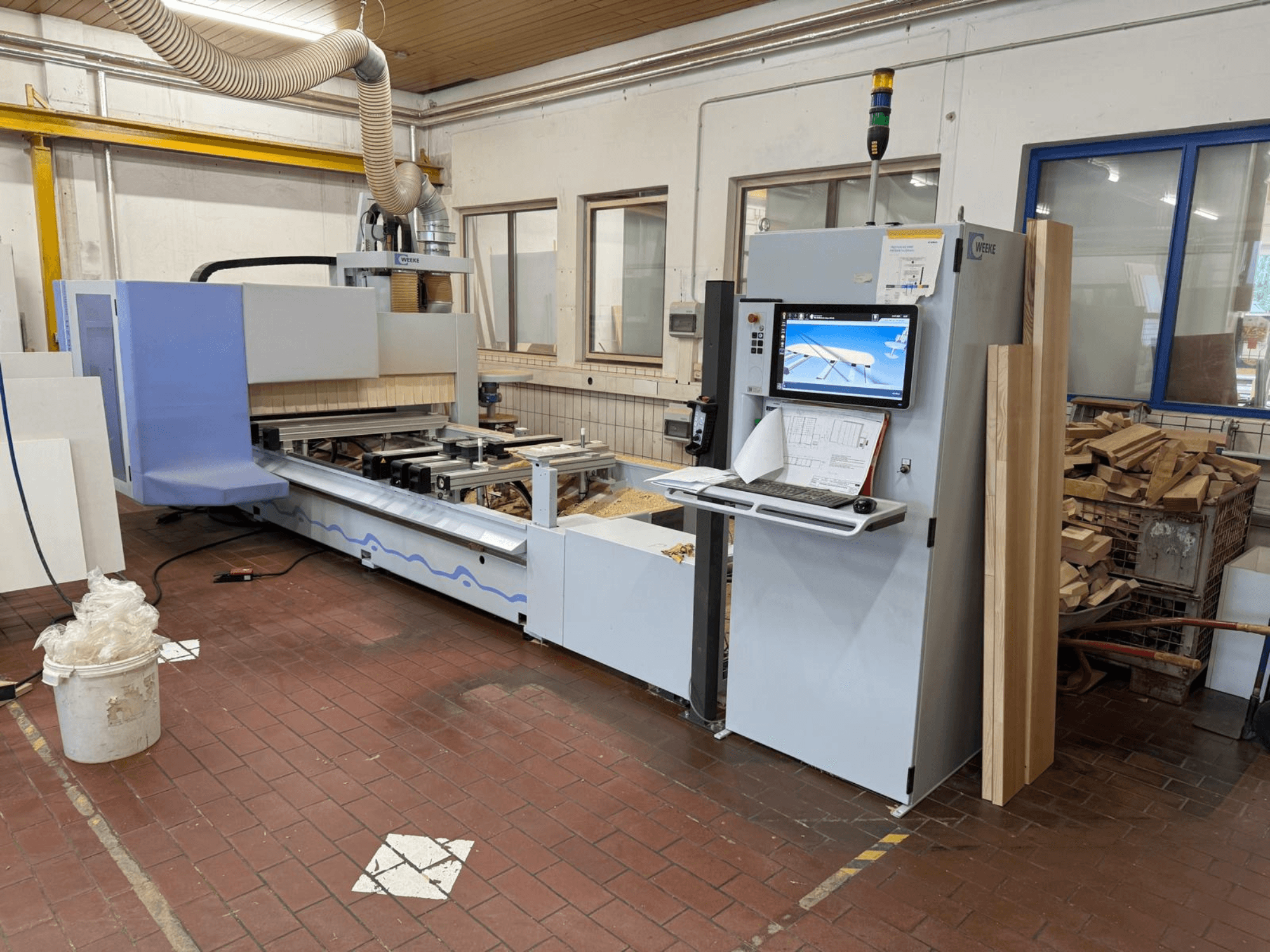 „Weeke PROFI BMG211/32/12/K“ CNC medžio apdirbimo centras, vaizdas iš priekio, su valdymo pultu ir medžio ruošiniais, su dulkių surinkimo sistema.