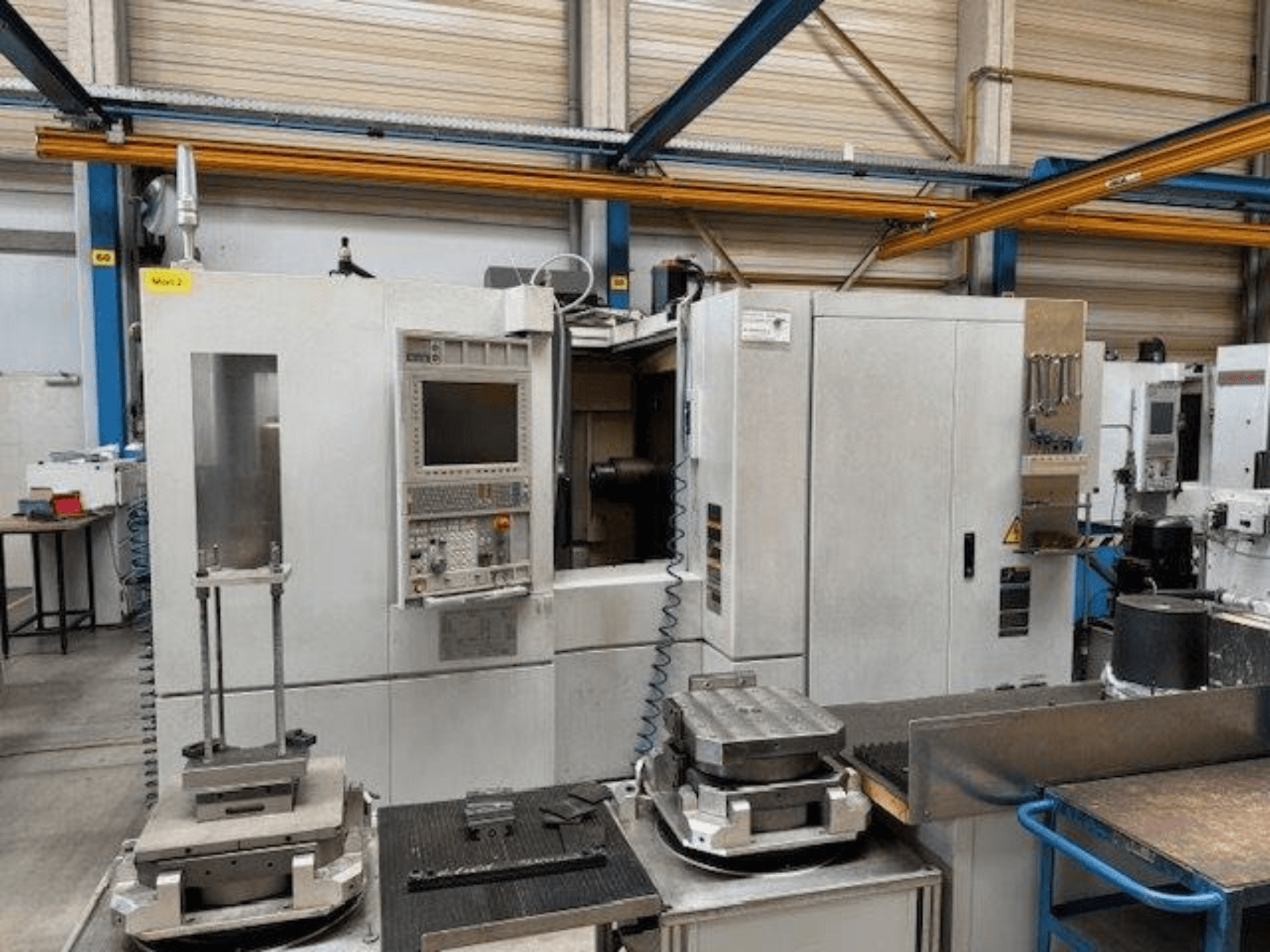 MORI SEIKI NH4000 DCG horizontalaus apdirbimo centro vaizdas iš priekio su valdymo pultu ir ant stalo esančiomis detalėmis.