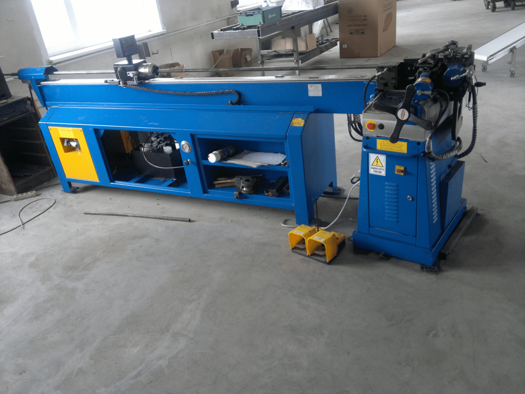 Mėlynos medžio apdirbimo staklės su geltonais akcentais, vaizdas iš šono; turi valdymo skydelį, kojinius pedalus ir besisukančių peilių mazgą.