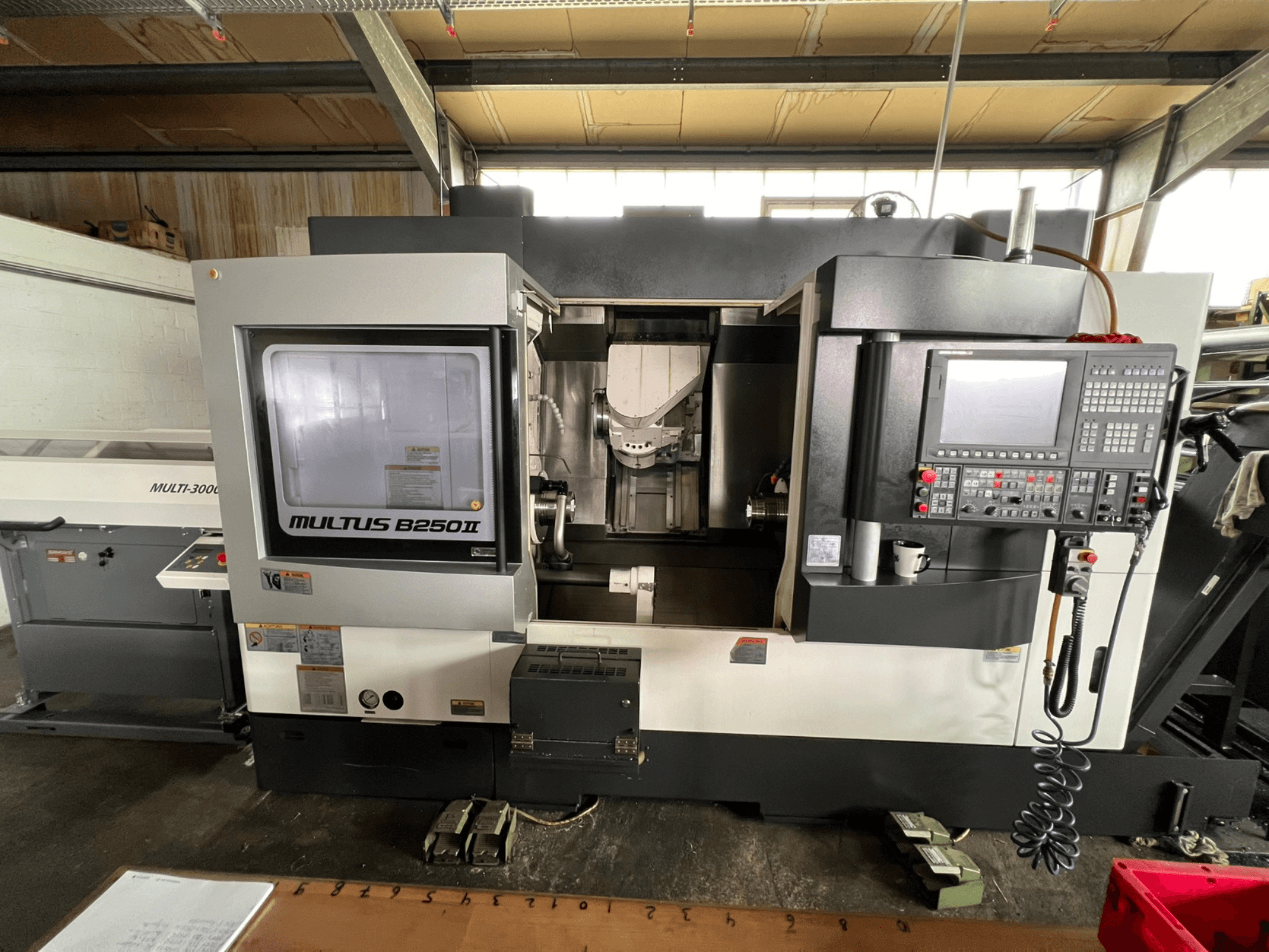 „Okuma Multus B250II MW“ tekinimo-frezavimo centras, vaizdas iš priekio, kuriame matomi valdymo skydelio ir apdirbimo zonos detalės.
