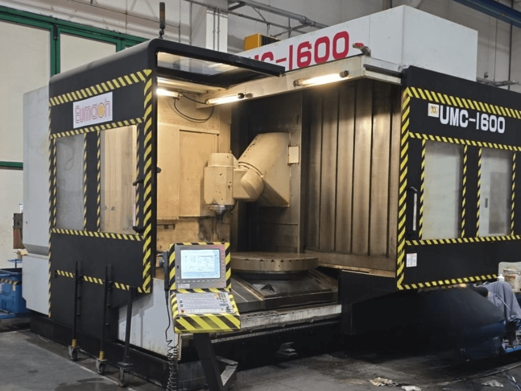 „Eumach UMC-1600“ vertikalusis apdirbimo centras, vaizdas iš priekio, kuriame matomi valdymo elementai ir apdirbimo zona su saugos juostomis.