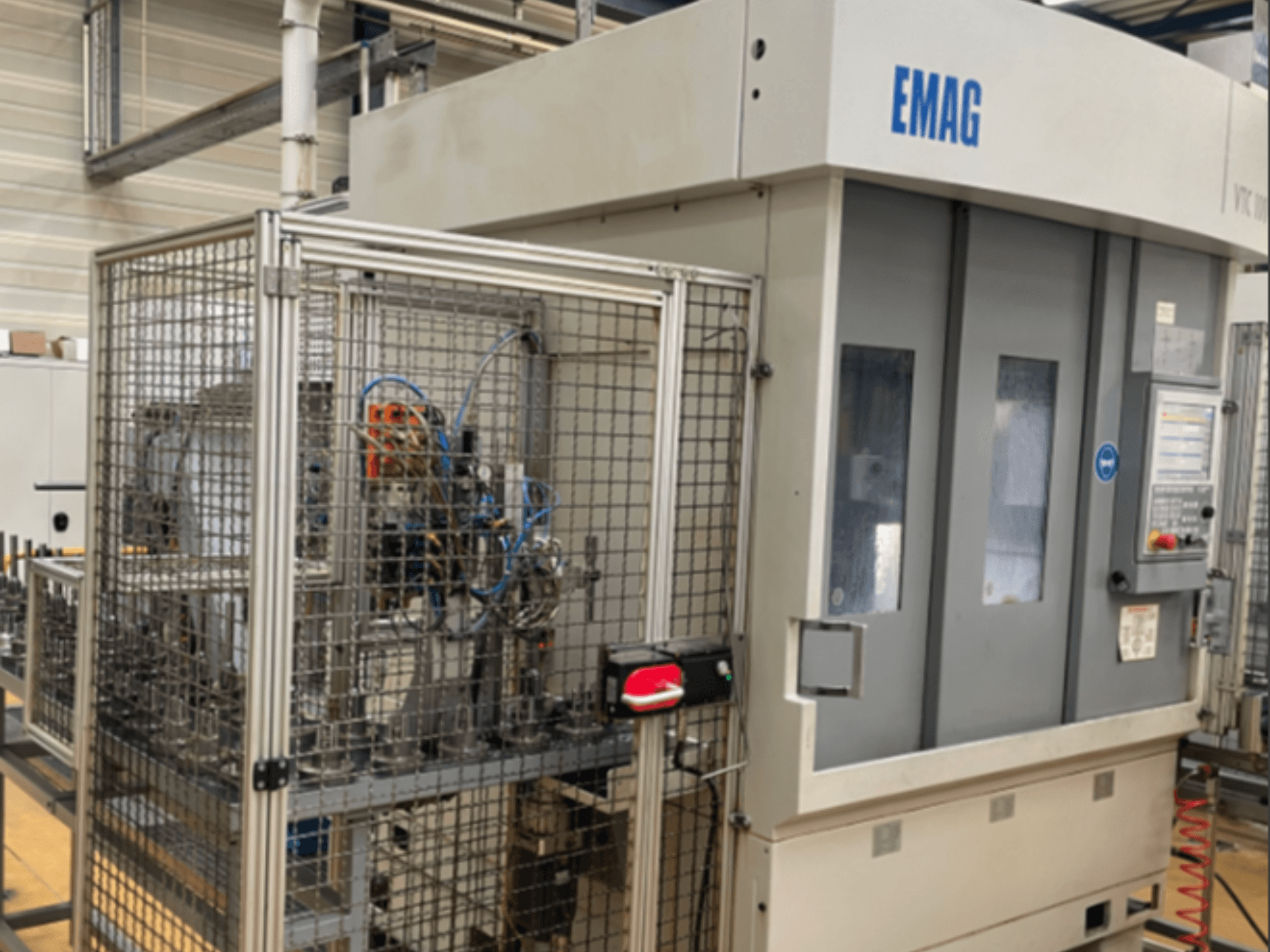 EMAG VTC 100 vertikaliojo tekinimo staklių vaizdas iš šono, kuriame matomi valdymo skydas ir apsauginių tvorelių detalės.