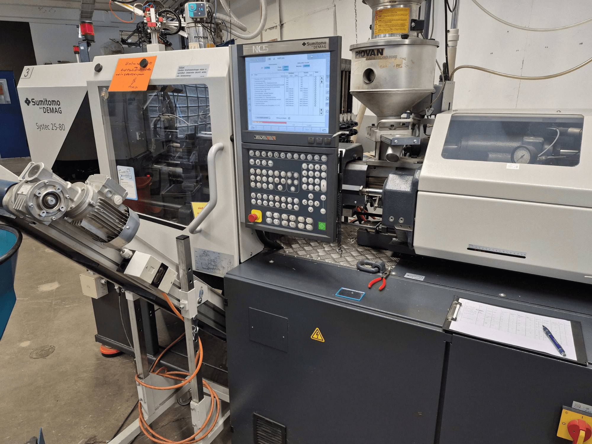 Hidraulinis liejimo staklės „SUMITOMO SHI DEMAG Systec 25/320-80“, vaizdas iš priekio, kuriame matomas valdymo pultas ir padavimo sistema.