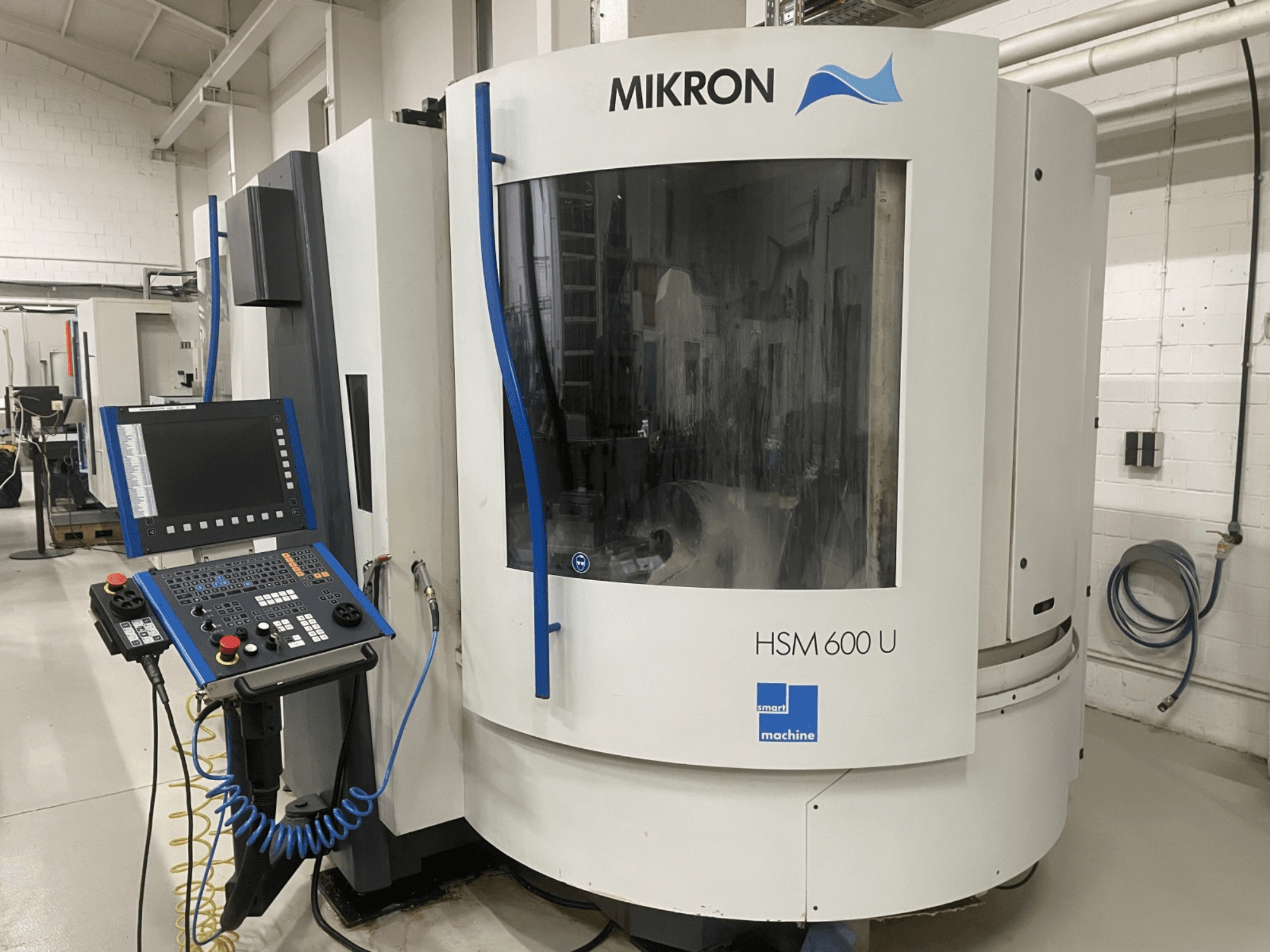 MIKRON HSM600U vertikalusis apdirbimo centras iš priekio, su valdymo skydeliu ir dideliu stebėjimo langu.