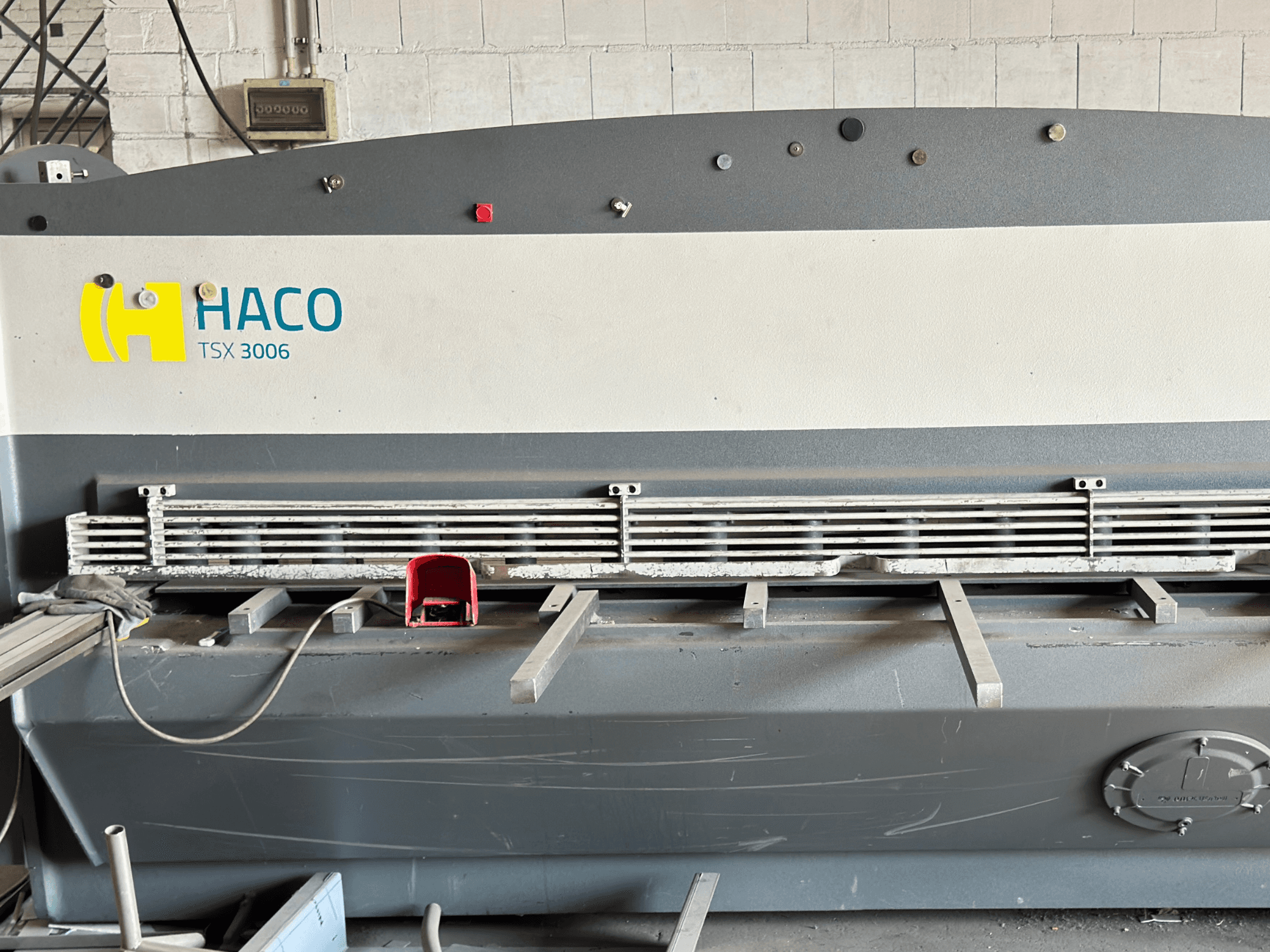 HACO TSX3006 MOT hidraulinės kirpimo staklės, vaizdas iš priekio, su metaliniais pjovimo peiliais ir valdymo skydeliu, kuriame matyti veikimo detalės.