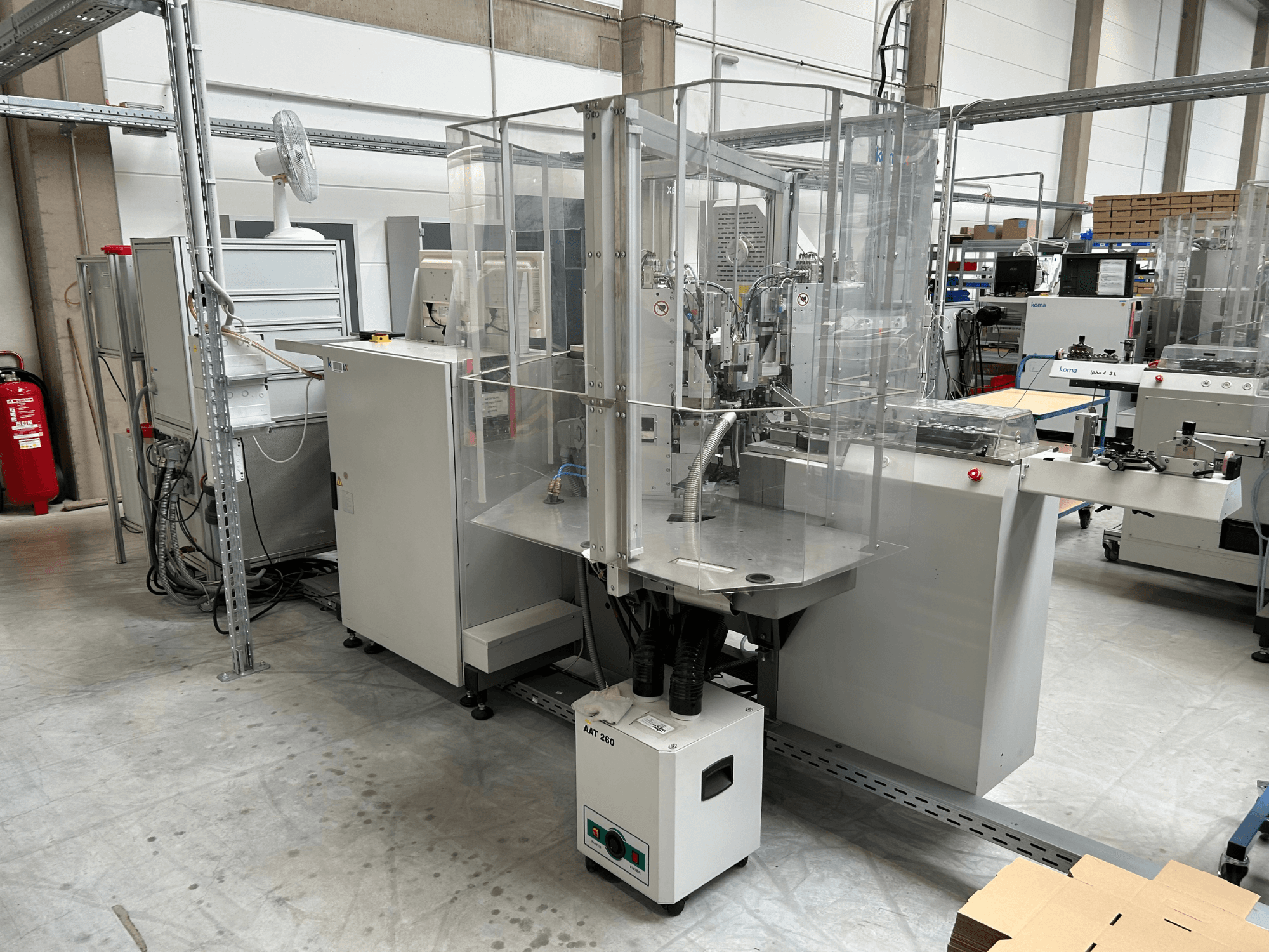 „KOMAX Alpha 433 L“ automatizavimo įranga gamykloje. Įranga turi skaidrų apsauginį gaubtą ir įvairius valdymo pultus.