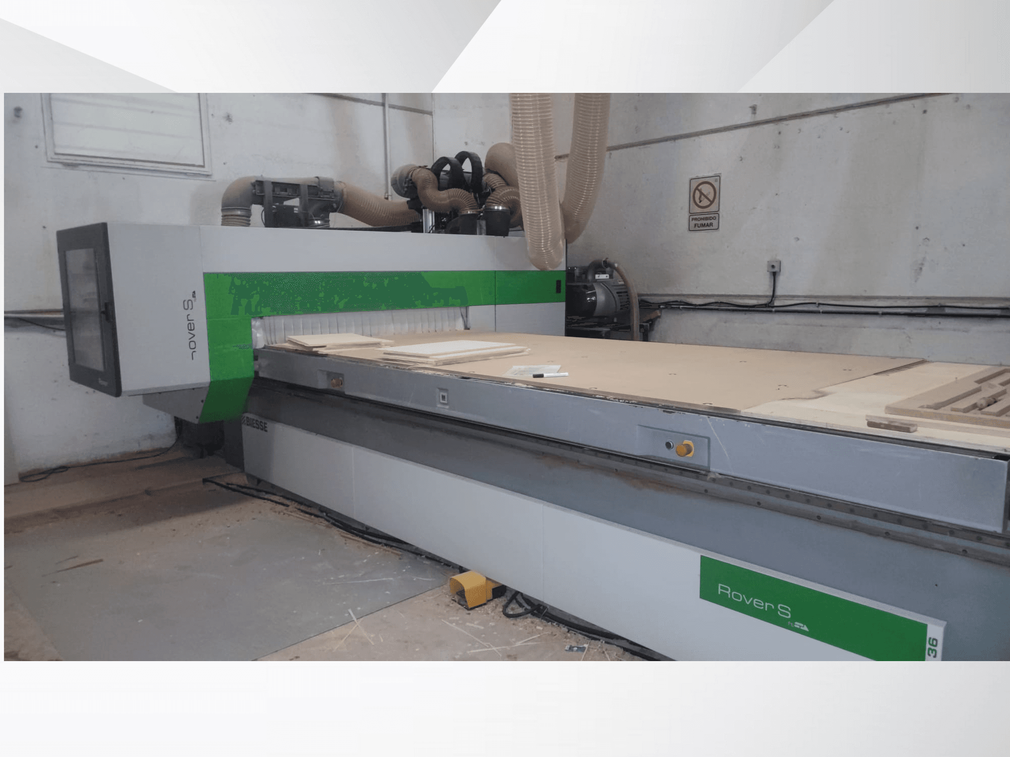 CNC staklių "Biesse Rover S", turinčių didelį darbo paviršių su medinėmis plokštėmis ir dulkių nusiurbimo žarnomis, vaizdas iš priekio.