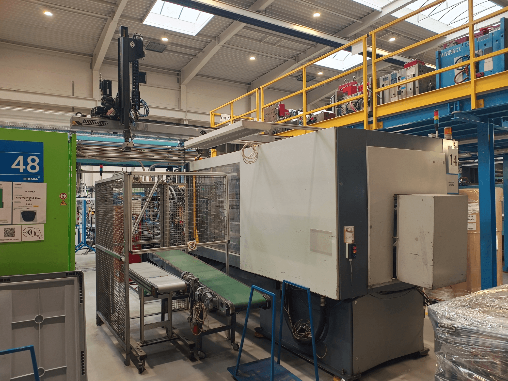 "Winmon" pramoninės automatikos mašina, šoninis vaizdas, kuriame matoma konvejerio juosta, valdymo skydelis ir apsauginis narvelis gamykloje.