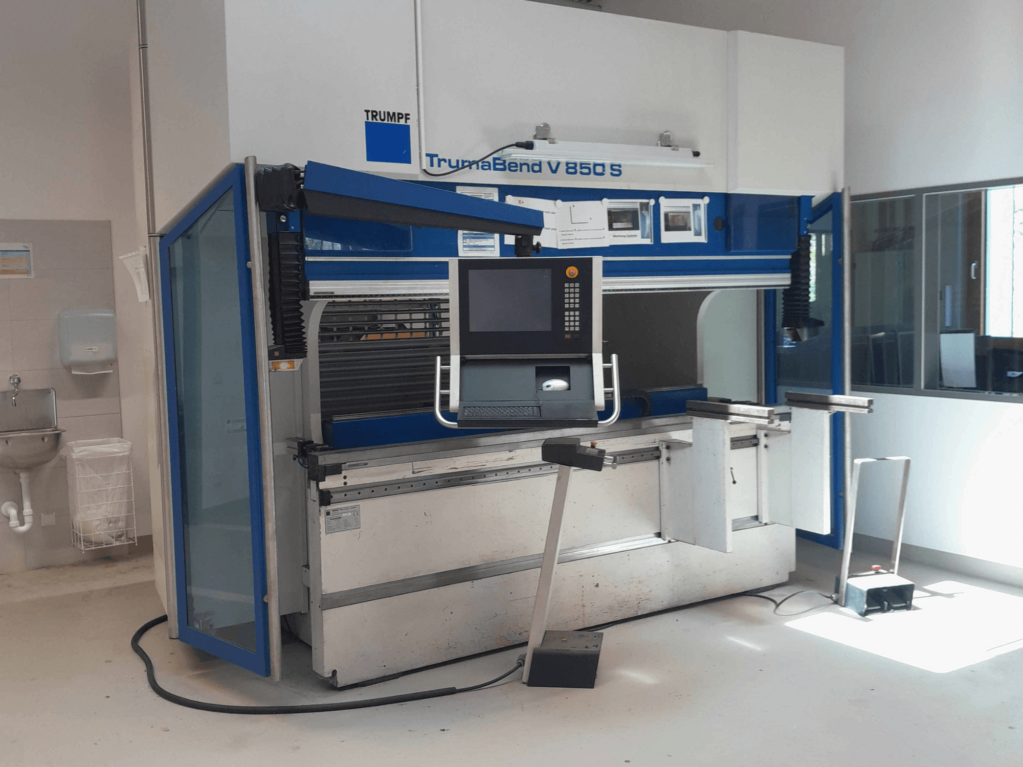 TRUMPF „TrumaBend V 850 S“ lenkimo presas, vaizdas iš priekio su valdymo pultu ir saugos įranga šviesioje darbo vietoje.