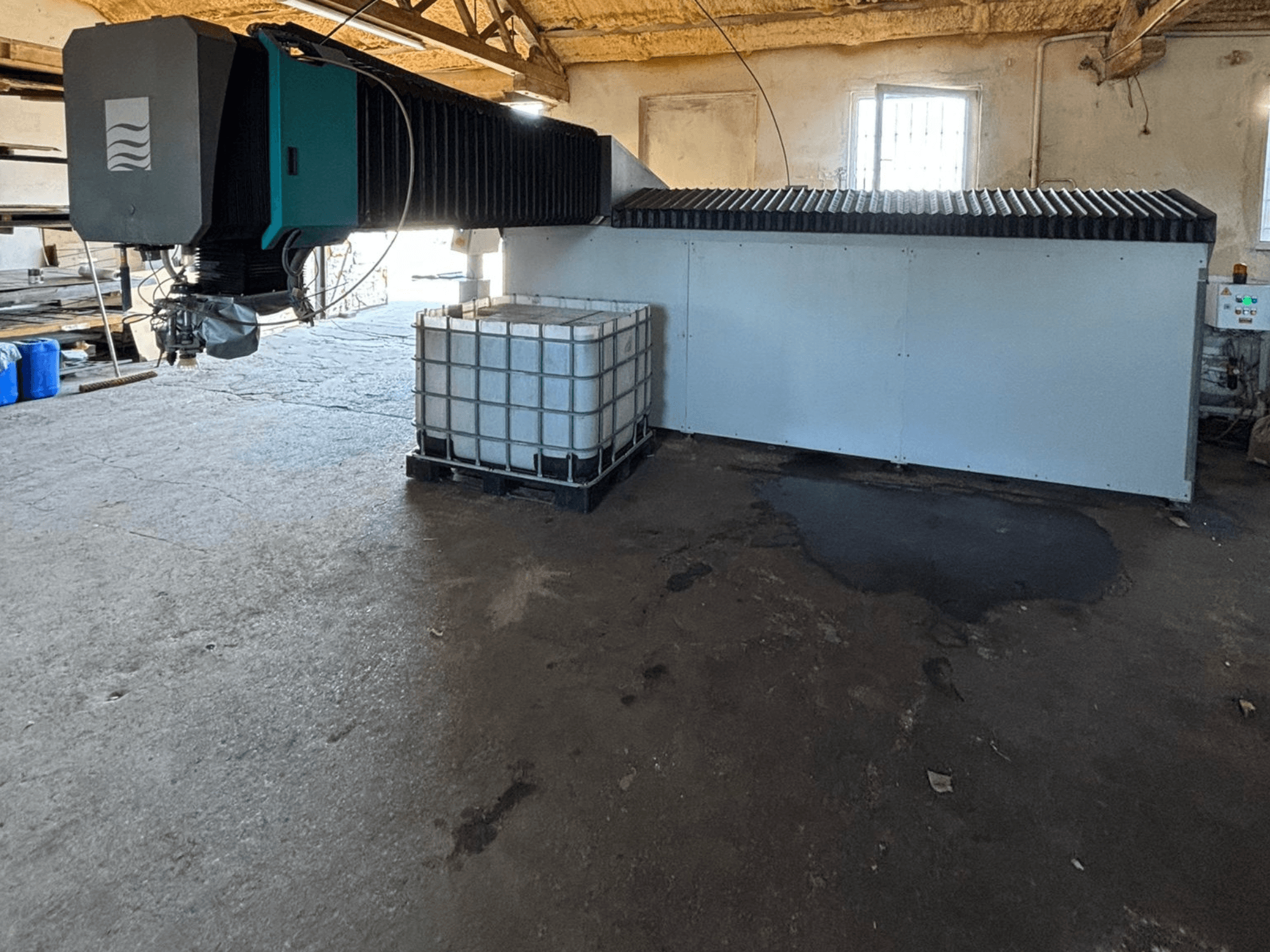 Pramoninė vandens srovės mašina dirbtuvėse, vaizdas iš šono, šalia matomas didelis vandens bakas ir valdymo skydelis.