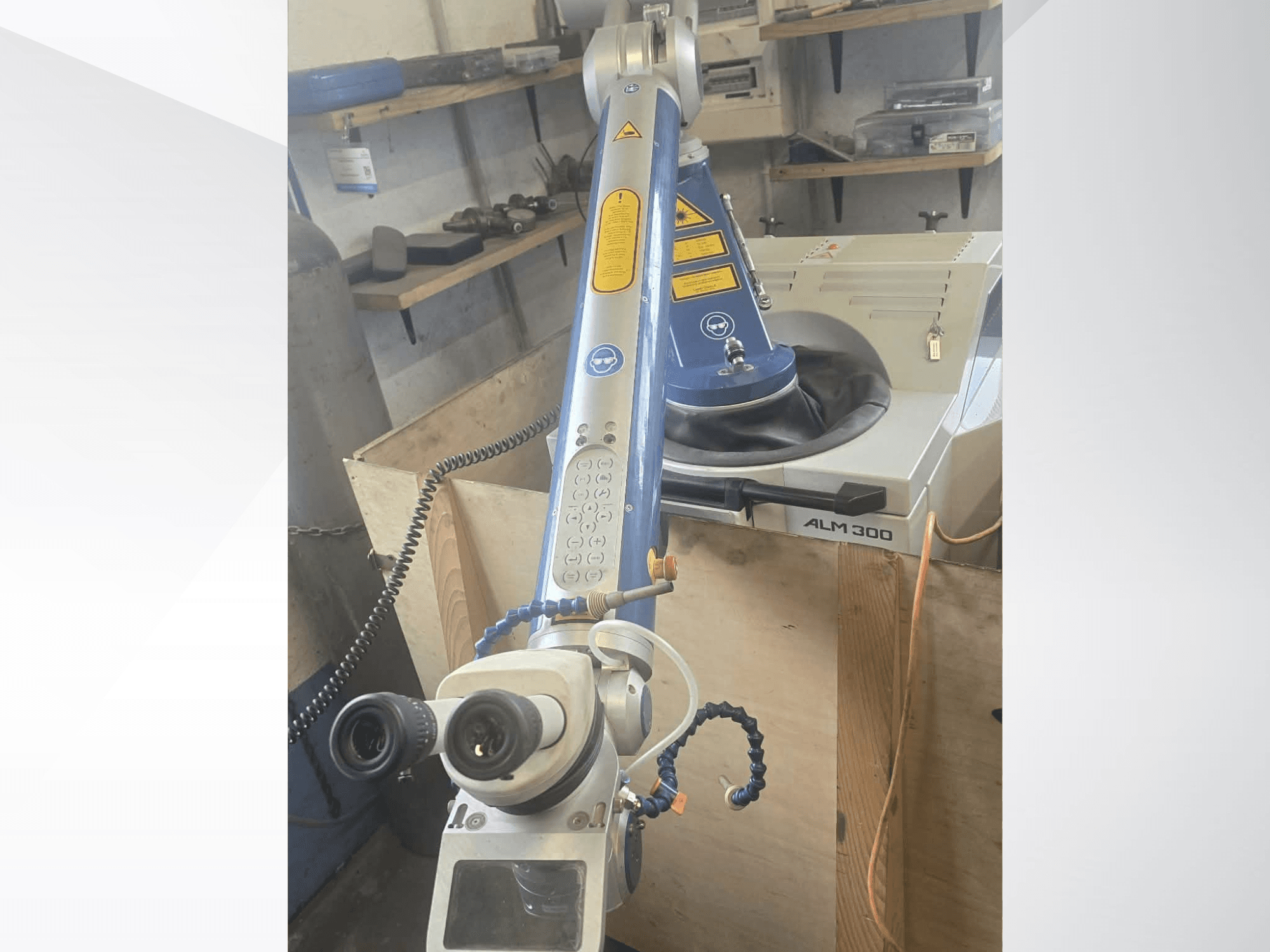 „ALPHA LASER ALM 300“ lazerinio suvirinimo staklių vaizdas iš priekio, kuriame matoma robotinė ranka, optiniai lęšiai ir valdymo pultas.