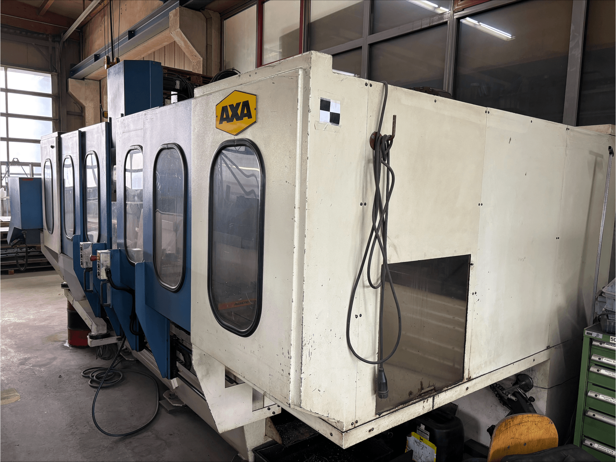 AXA VSC-1-M/C vertikalusis apdirbimo centras, vaizdas iš priekio, didelis baltas korpusas ir mėlynas valdymo skydelis.