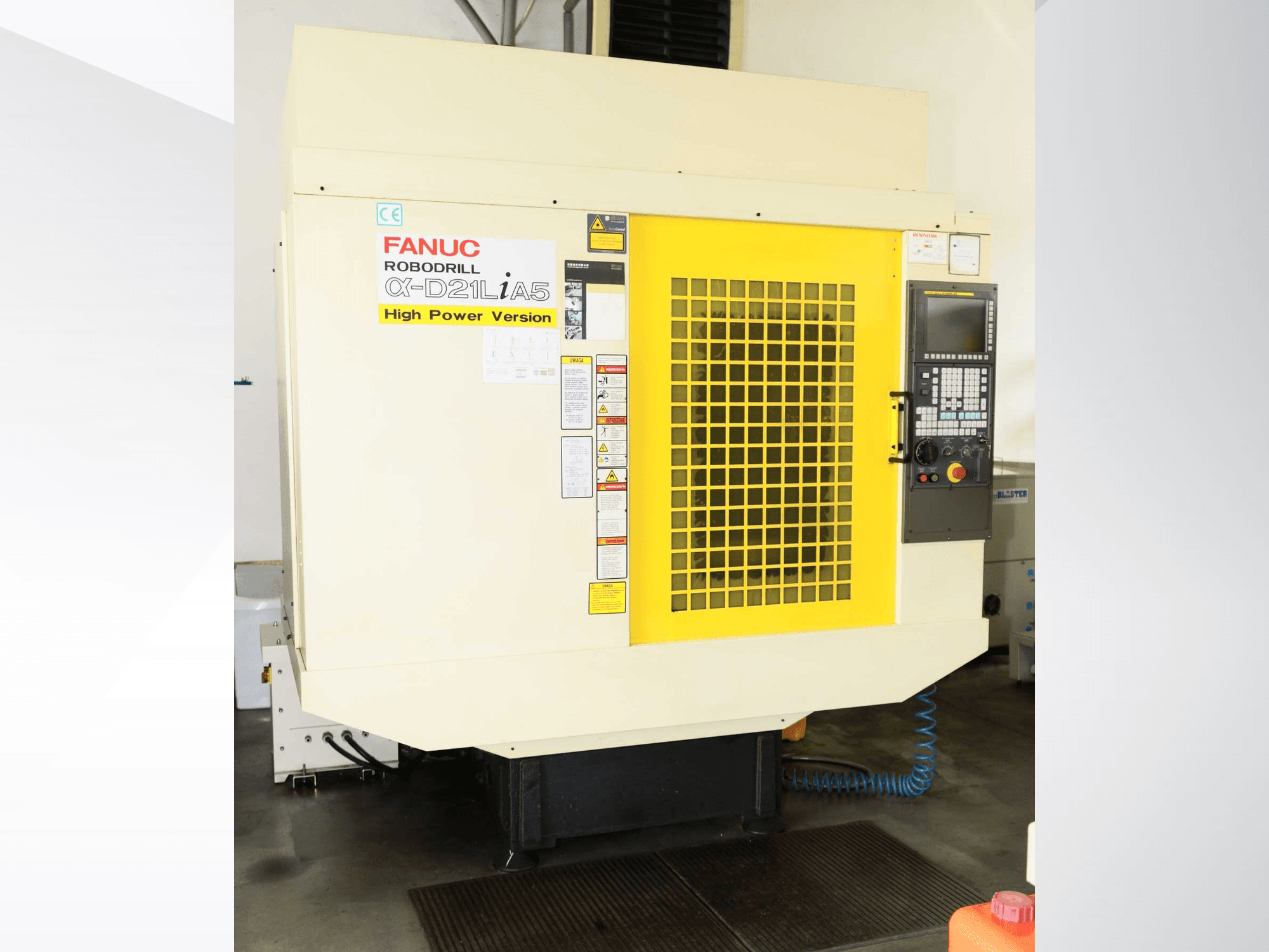 Vertikalusis apdirbimo centras „FANUC ROBODRILL α-D21LiA5“, vaizdas iš priekio su geltonu apsauginiu groteliu ir valdymo skydo detalėmis.