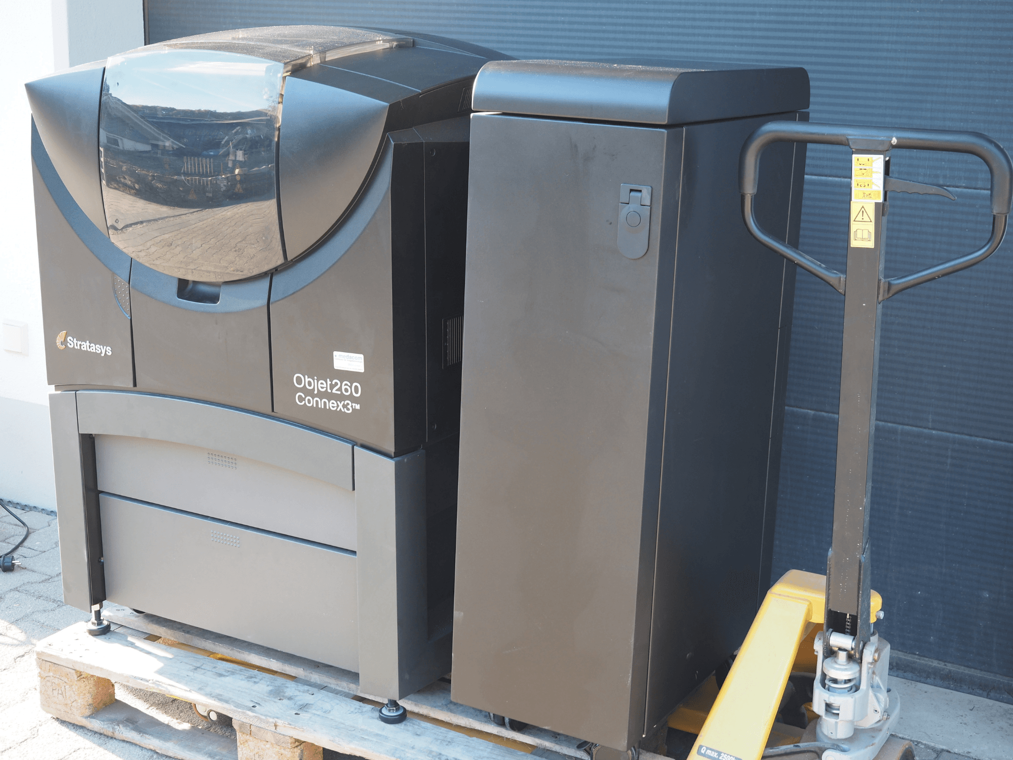 "Stratasys Objet260 Connex3" plastikinis 3D spausdintuvas, vaizdas iš šono, kompaktiškas dizainas su valdymo skydeliu ir prijungta medžiagų talpykla.
