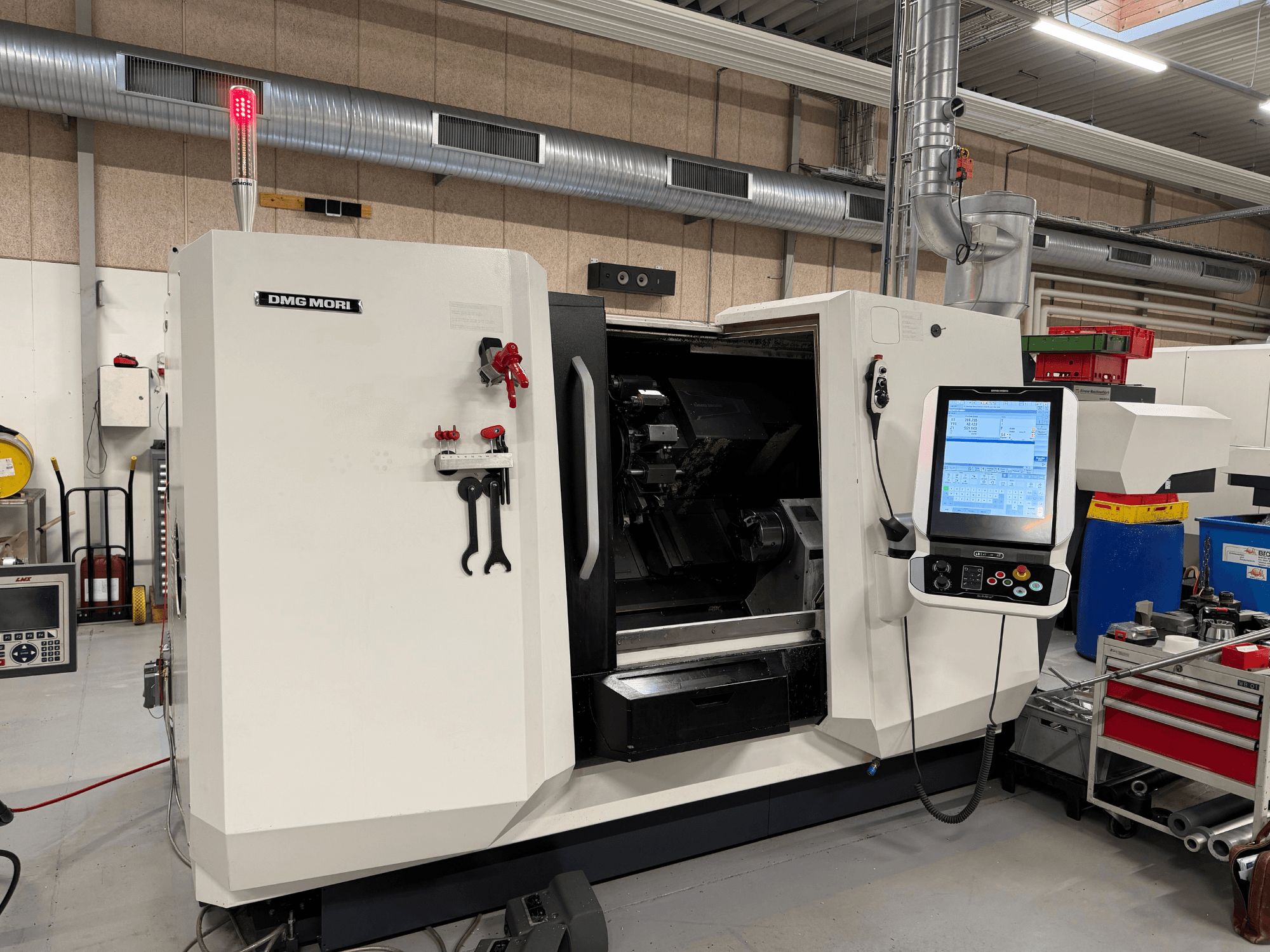 DMG MORI CLX 450 V6 horizontalusis tekinimo staklės, vaizdas iš priekio, kuriame matomas valdymo pultas, avarinio sustabdymo mygtukas ir saugos lemputė.