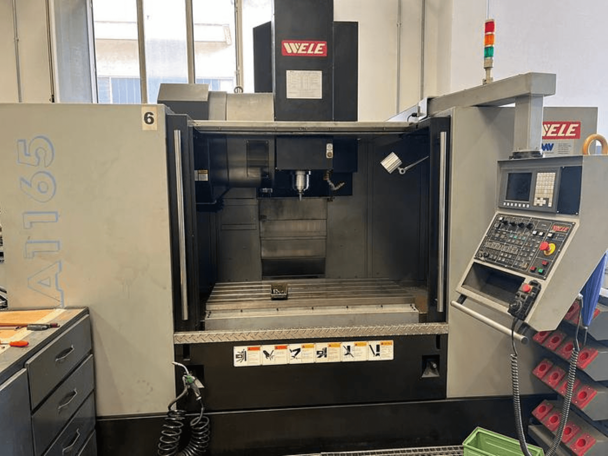 WELE A165 CNC apdirbimo centras, vaizdas iš priekio, matomas valdymo skydelis, įrankių laikiklis ir darbo stalas. Pramoninė aplinka.