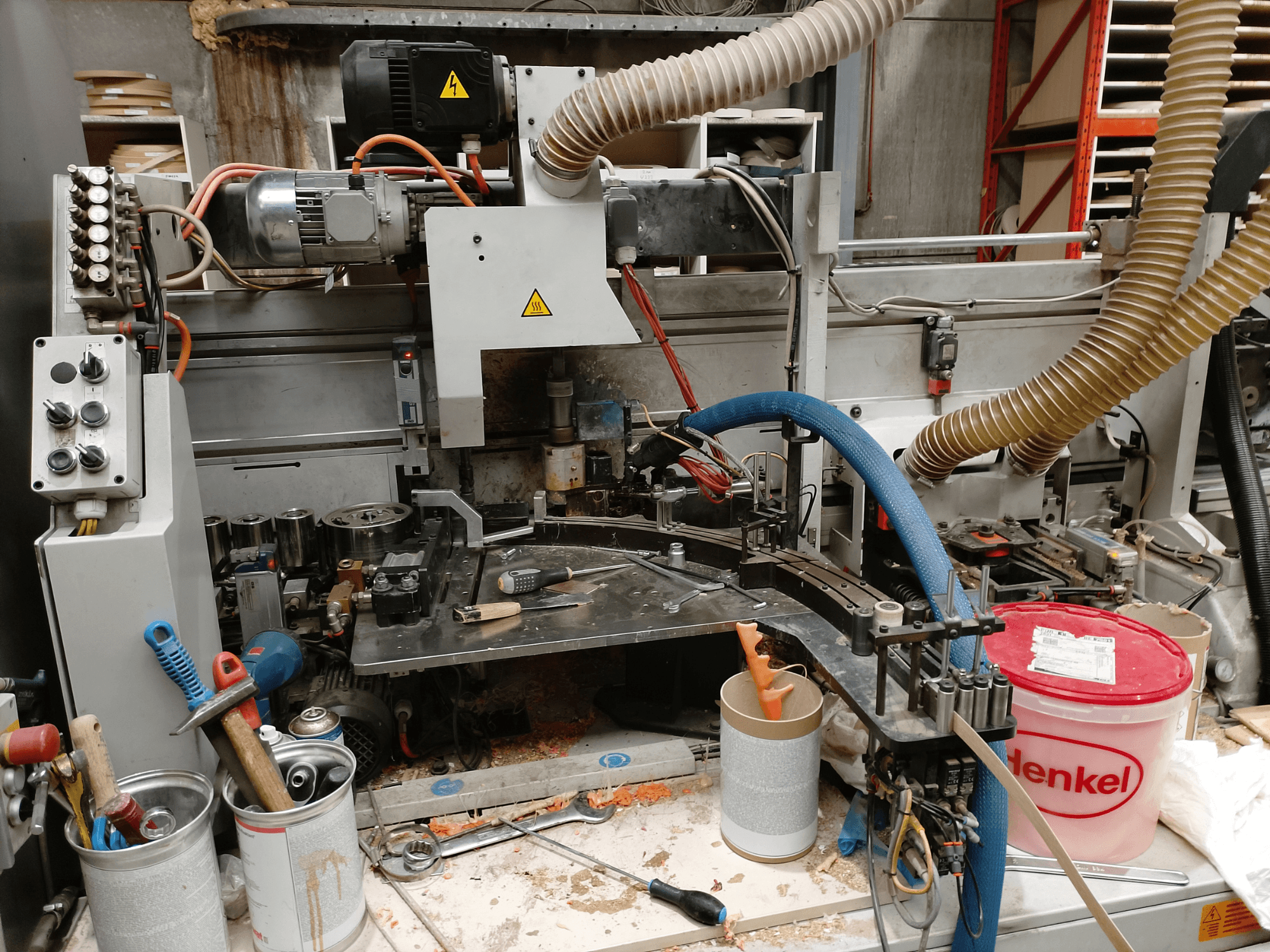 BIESSE Edge Stram B1 briaunų apdirbimo staklės iš priekio, kuriose tarp medžio drožlių matyti mašinos, žarnos ir darbo įrankiai.