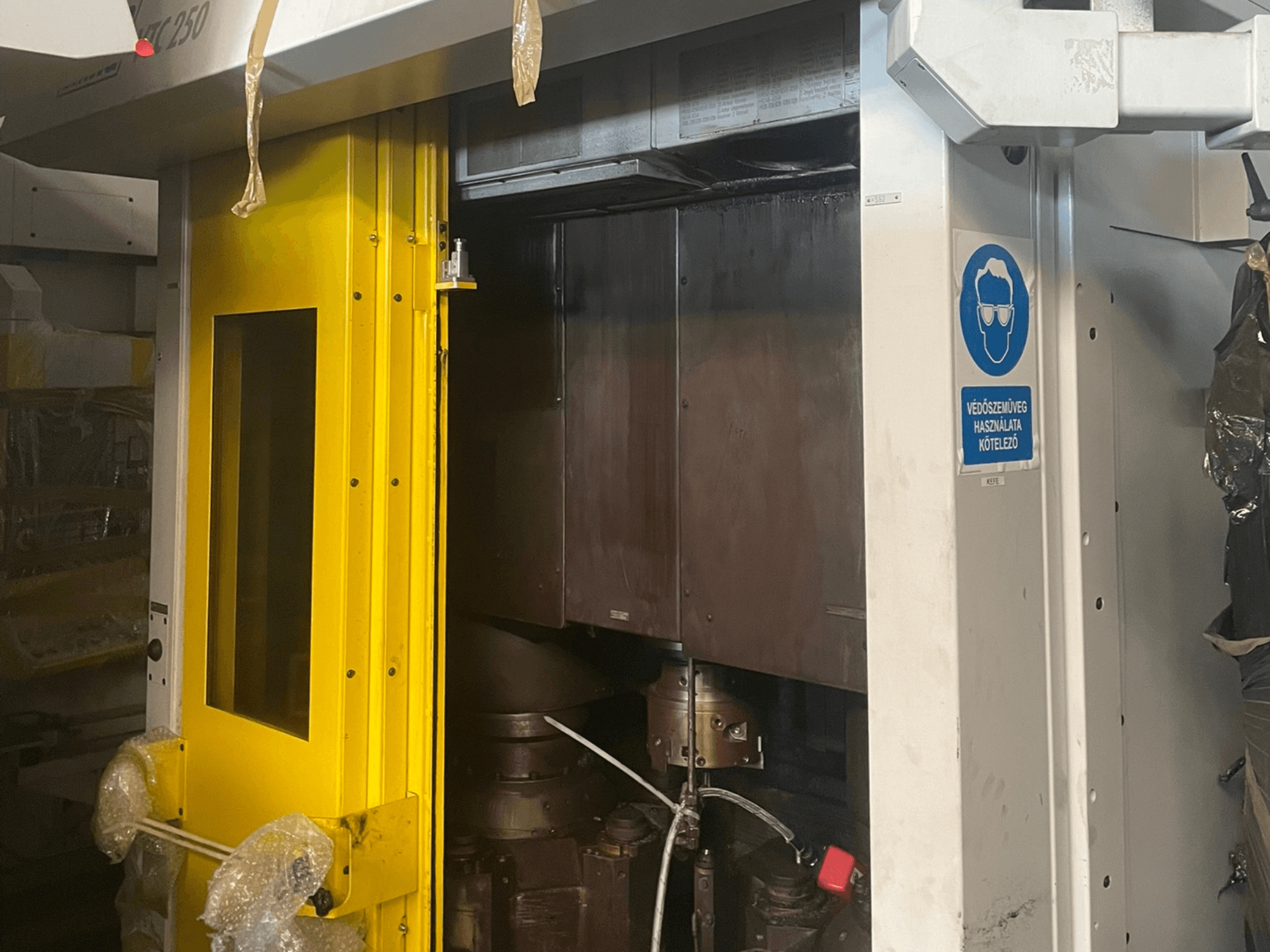 Geltonos mašinos įėjimo durys su saugos ženklu, pramoninės Z250 modelio mašinos priekinis vaizdas, kuriame matyti vidiniai komponentai.