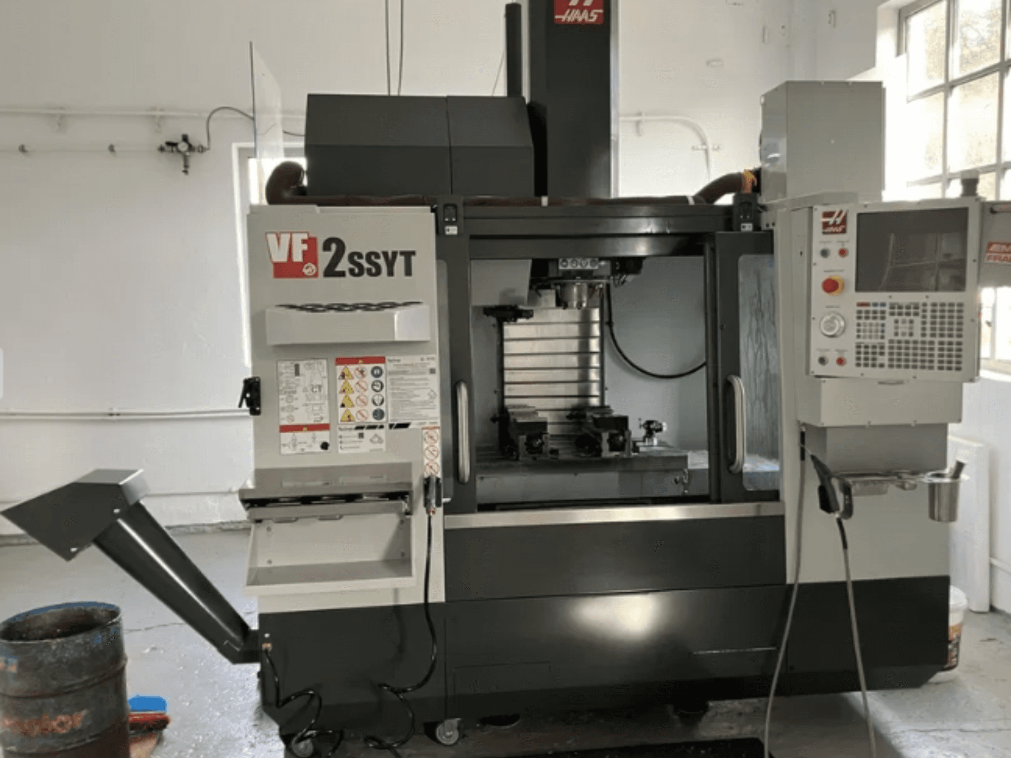 "Haas VF-2SSYT" CNC frezavimo staklės, vaizdas iš priekio, su valdymo skydeliu, įrankių laikikliu ir aušinimo skysčio sistema, skirta metalo apdirbimui.