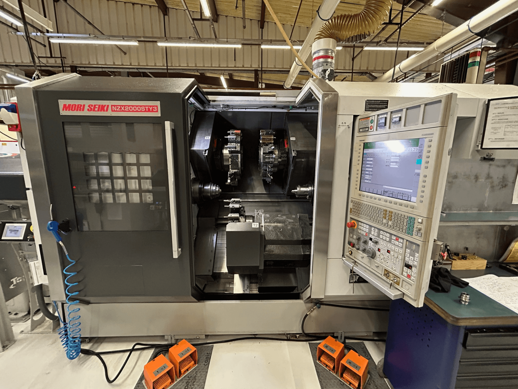 Daugiaspindulinis tekinimo staklės „MORI SEIKI NZ2000 ST3Y3“, vaizdas iš priekio, kuriame matomas valdymo pultas ir apdirbimo zona.
