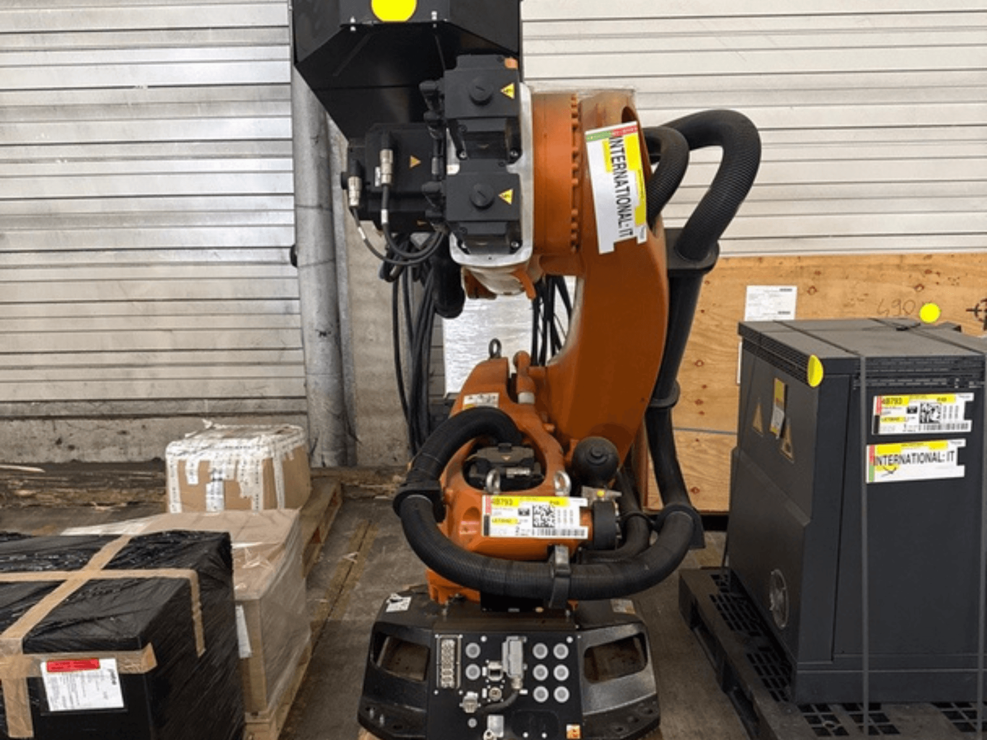 „KUKA KR 210 R2700 extra“ roboto ranka, vaizdas iš priekio; eksponuojama ant padėklo šalia pakuočių ir įrangos.