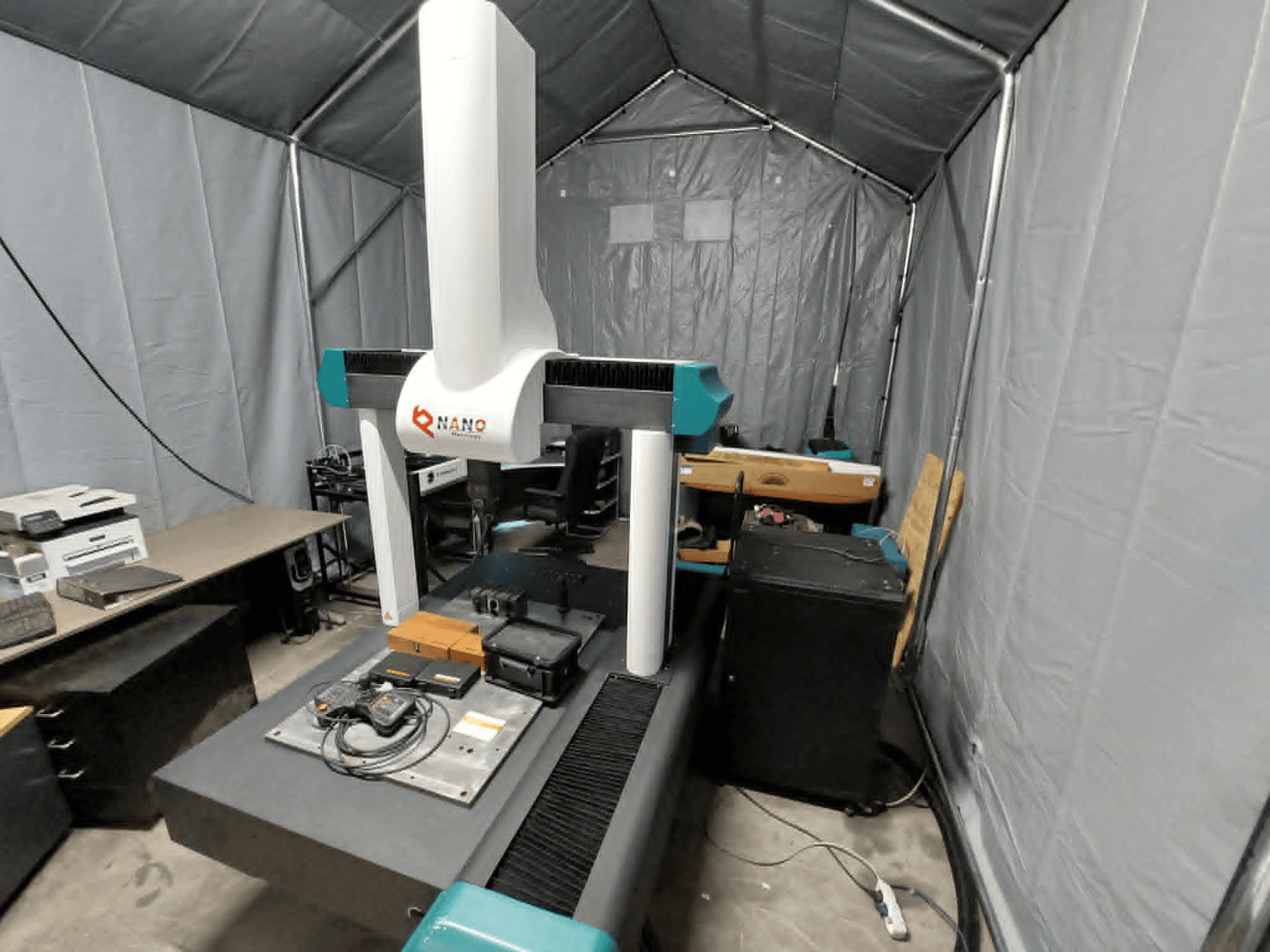 NANO METROLOGY Micr 7106 CMM palapinėje; iš priekio matoma mašinos rankena ir matavimo platforma su priedais.