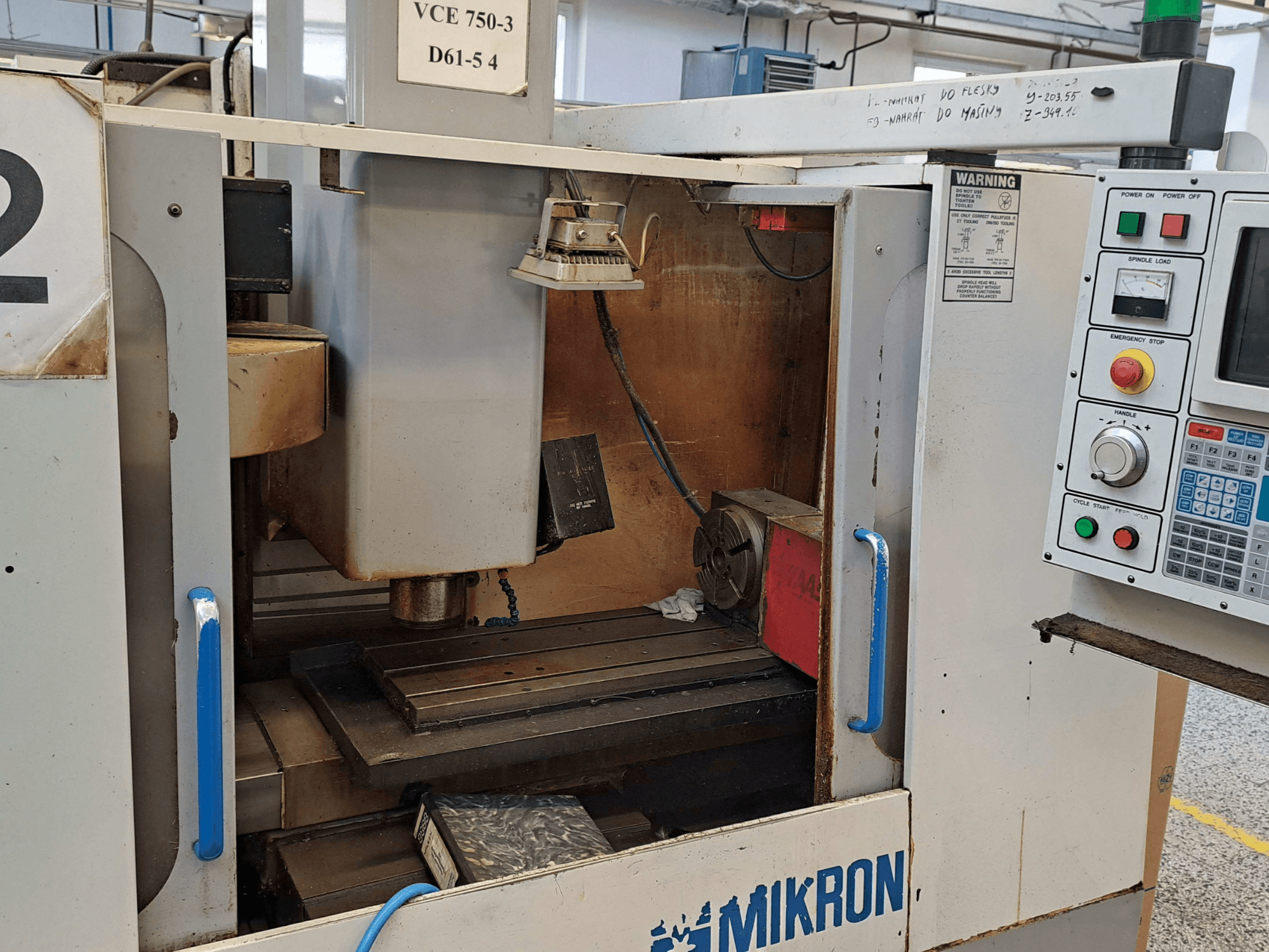 Frezavimo staklių "Mikron VCE 750-3" priekinis vaizdas, kuriame matyti suklys, valdymo skydelis ir stalas su techninėmis detalėmis.