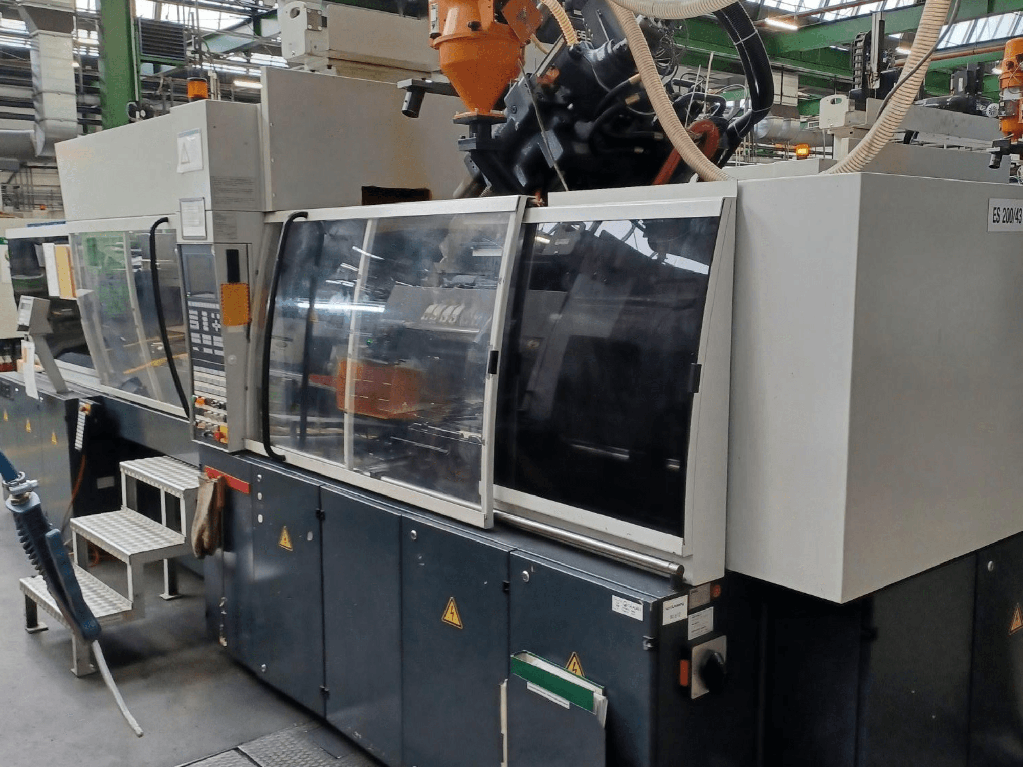 Nežinomo prekės ženklo ir modelio plastiko liejimo mašinos su permatomomis apsauginėmis durelėmis ir valdymo skydeliu vaizdas iš priekio.