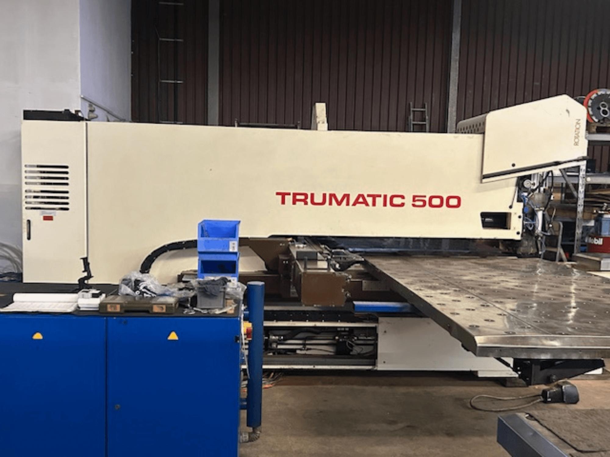 TRUMPF TRUMATIC 500 CNC perforavimo staklės, vaizdas iš priekio, su valdymo pultu ir dideliu darbo stalu, ant kurio matomas perforuotas paviršius.