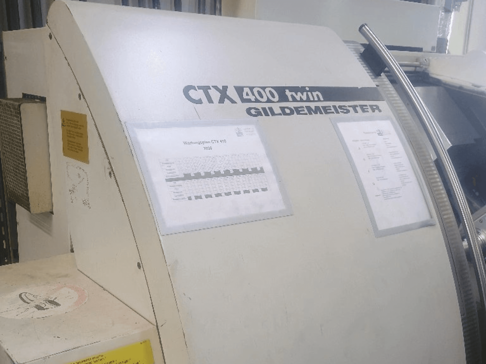 „Gildemeister CTX 400“ dviguba horizontali tekinimo staklė, vaizdas iš priekio, kuriame matomi valdymo pultai ir techninė dokumentacija.