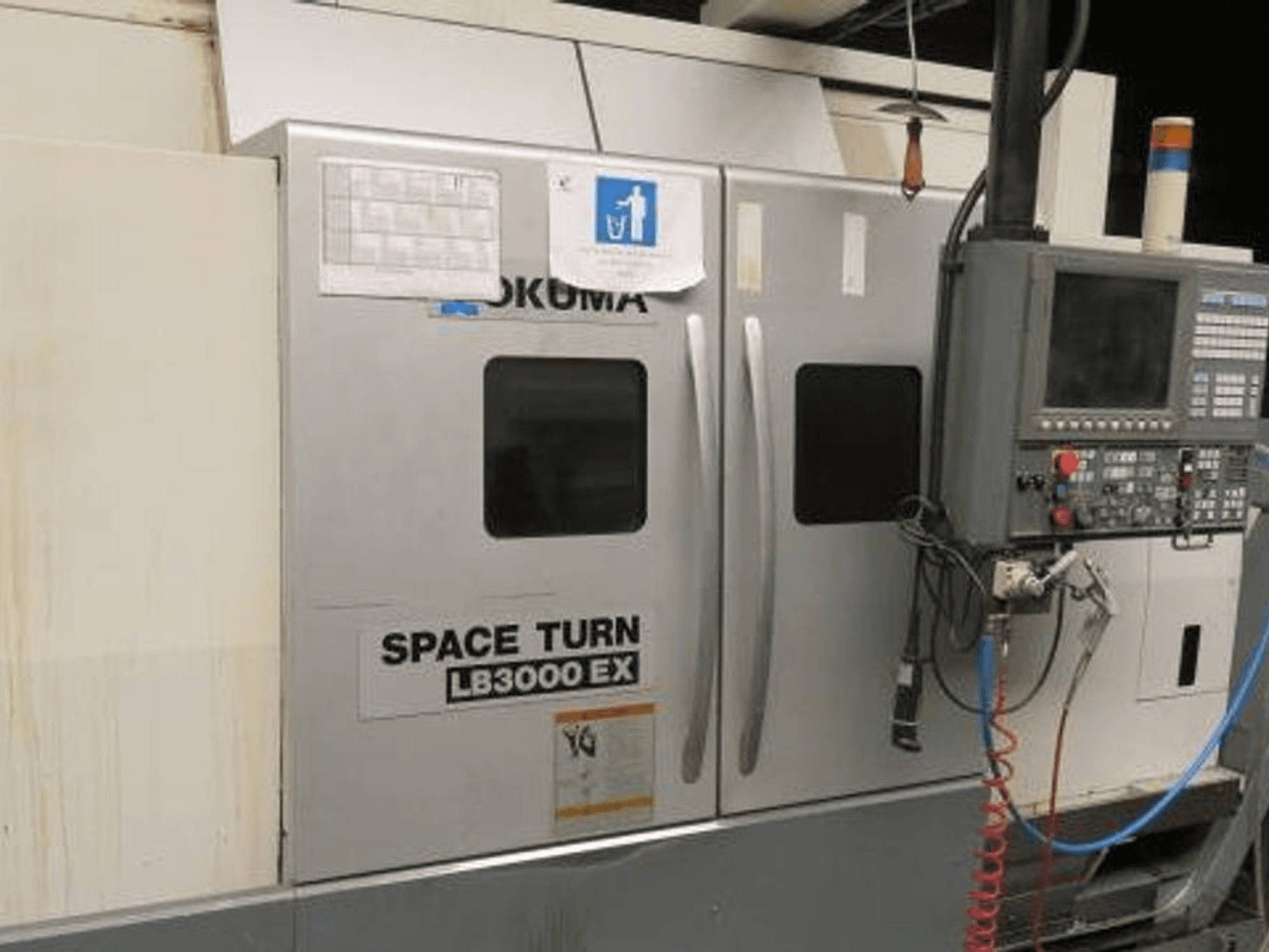 Okuma Space Turn LB3000 EX CNC staklės, vaizdas iš šono, su valdymo skydeliu, dvejomis durelėmis ir matomais laidais.