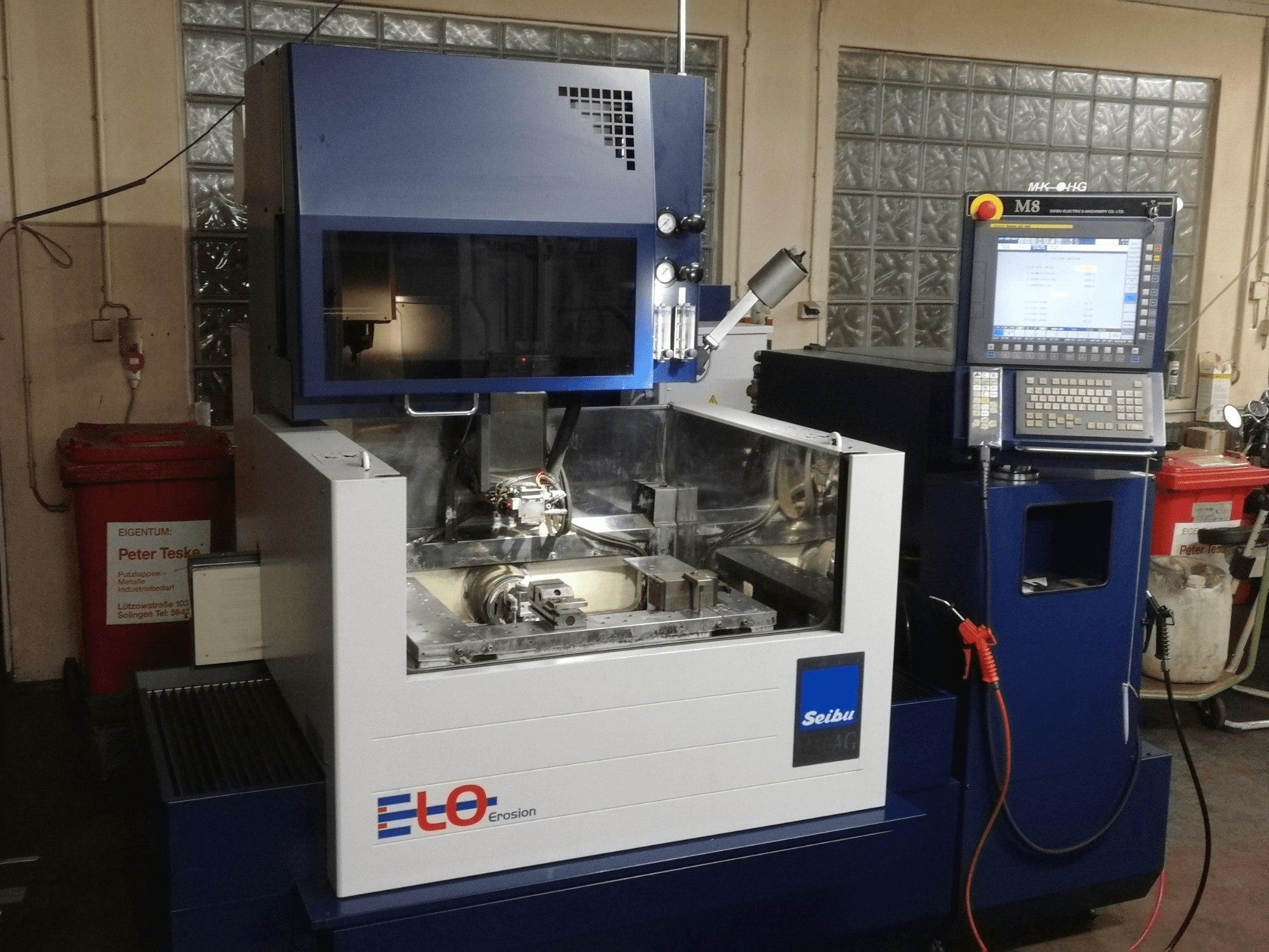 ELO Seibu erozijos mašina iš priekio, su valdymo skydeliu ir matoma darbo zona su metaliniais komponentais.