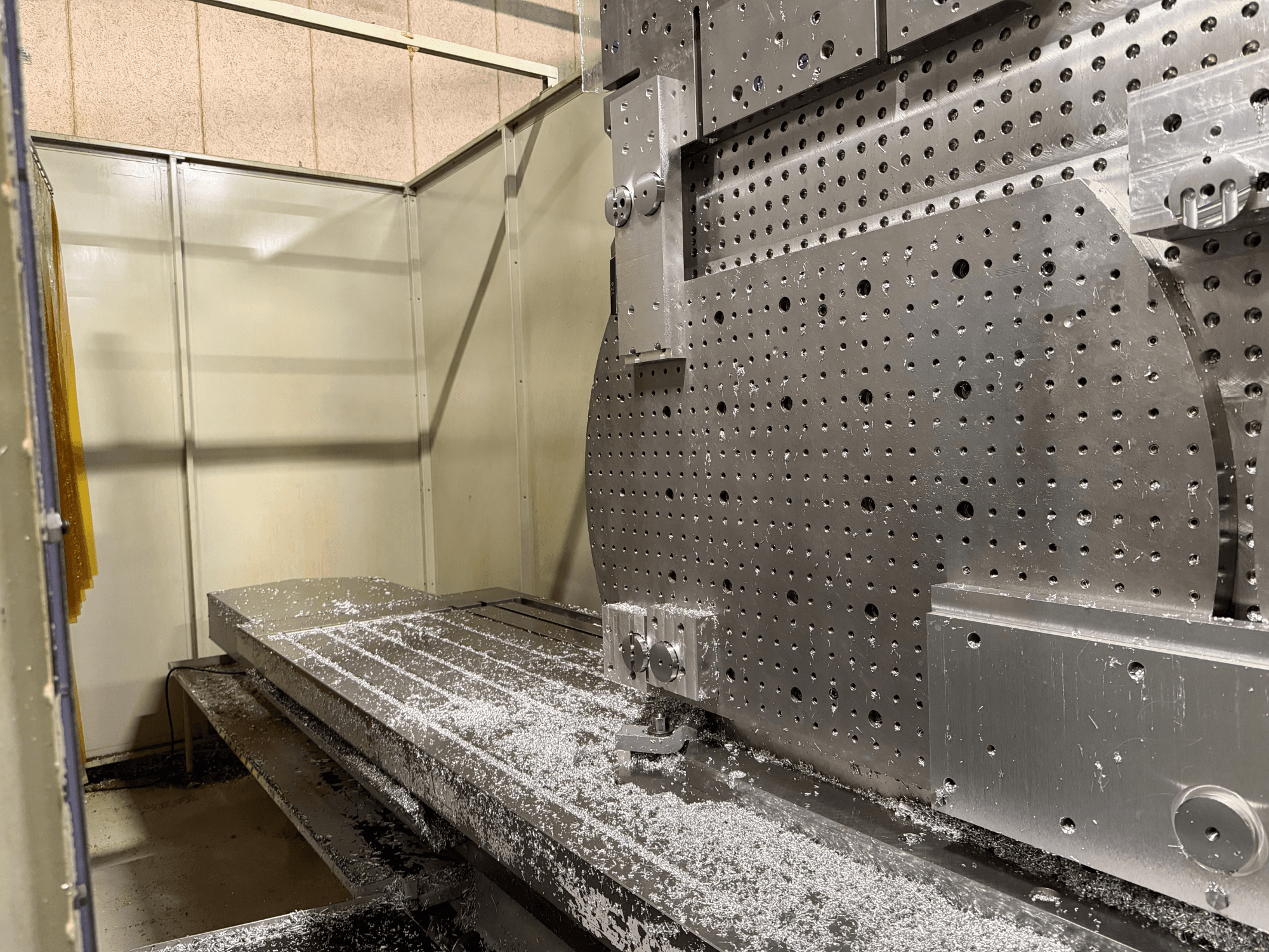 Universalaus apdirbimo centro KIHEUNG KNC-U1000 priekinis vaizdas iš arti, ant metalinio darbo stalo matomos aliuminio drožlės.