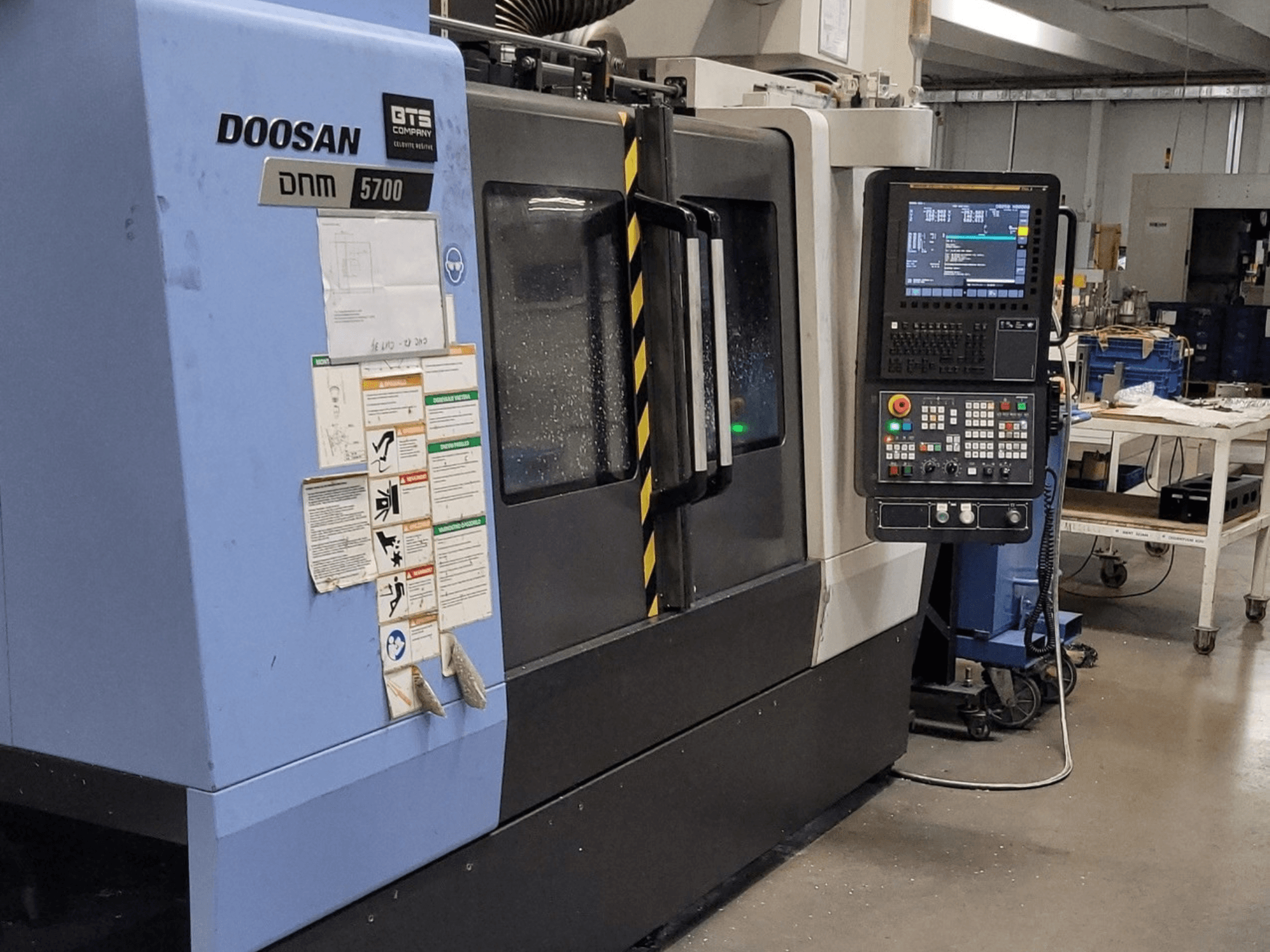 Vertikalusis apdirbimo centras „DOOSAN DNM 5700“, vaizdas iš priekio, kuriame matomas valdymo skydas ir valdymo elementai.
